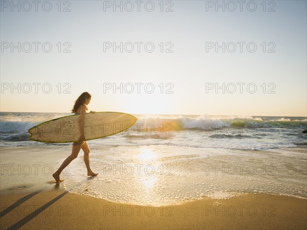 Mixed race woman carrying surfboard on beach