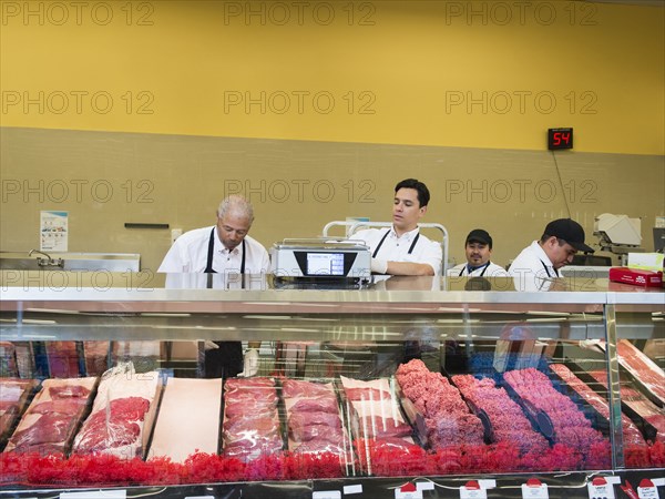 Butchers at meat counter of grocery store
