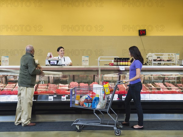 Butcher serving customers at meat counter of grocery store