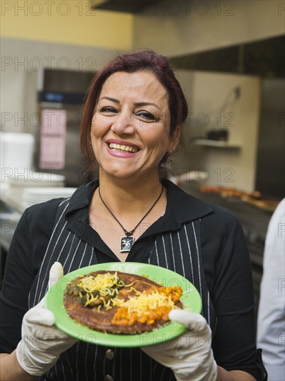 Mixed race chef holding plate of food in kitchen