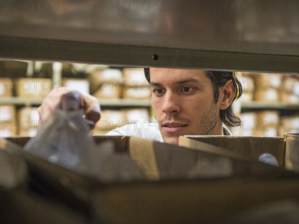 Mixed race worker examining bin in textile factory