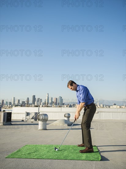 Caucasian businessman playing golf on urban rooftop