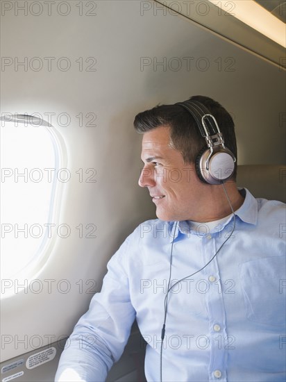 Caucasian businessman listening to headphones on airplane
