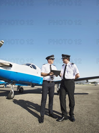 Caucasian pilots using digital tablet on runway