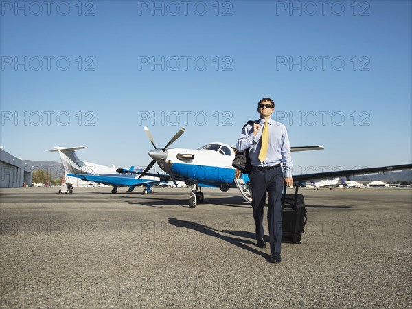 Caucasian businessman rolling luggage on runway