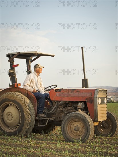 Caucasian farmer driving tractor in crop field