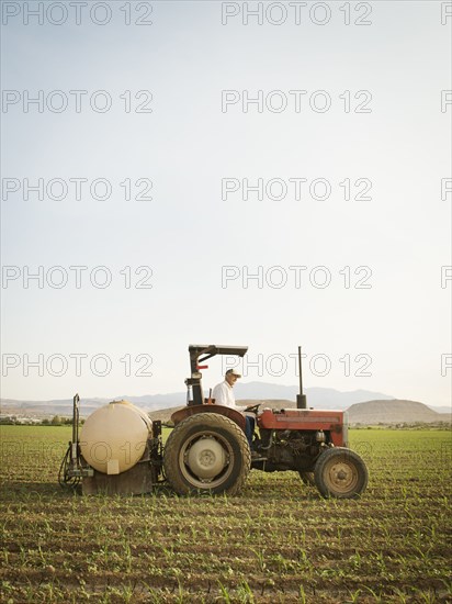 Caucasian farmer driving tractor in crop field