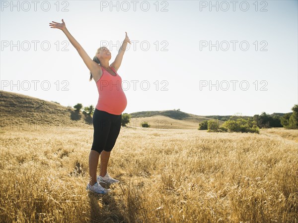 Pregnant Hispanic woman cheering in rural landscape