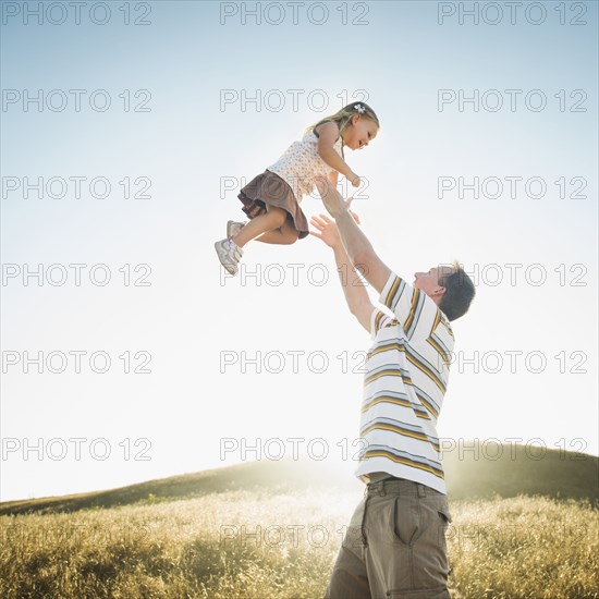 Caucasian father lifting daughter overhead in rural field