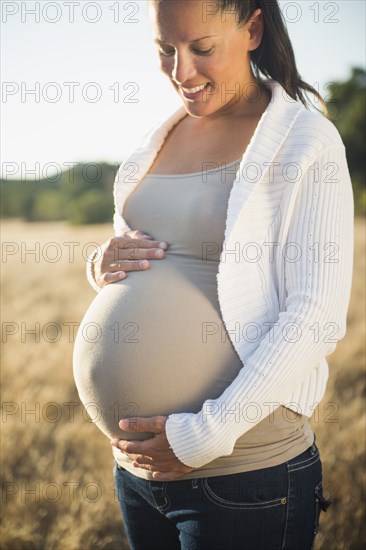 Pregnant Hispanic mother holding stomach in field
