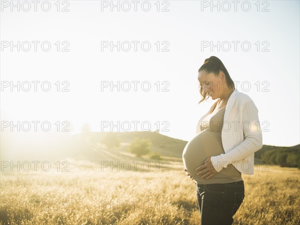 Pregnant Hispanic mother holding stomach in rural field