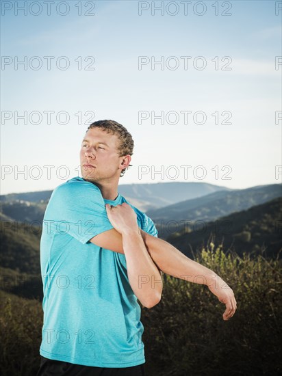 Caucasian man stretching on hilltop