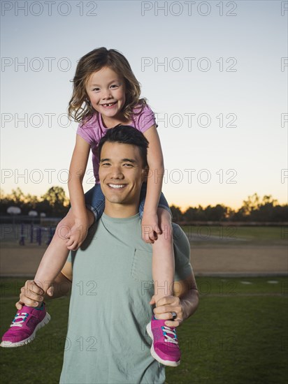 Father carrying daughter on shoulders in park