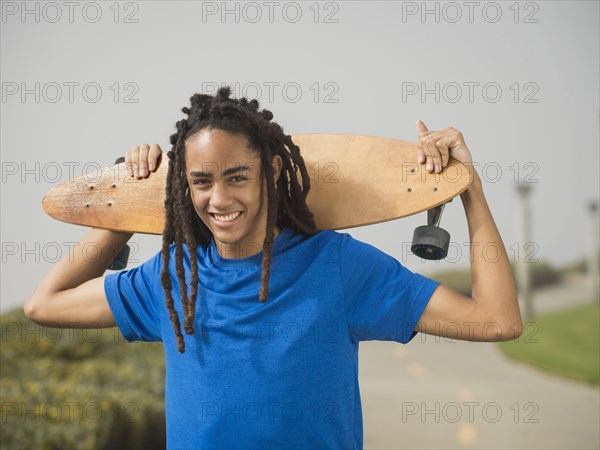 Black teenage boy carrying skateboard on street