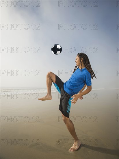 Black teenage boy playing with soccer ball on beach