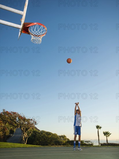 Black teenage boy shooting basketball on court