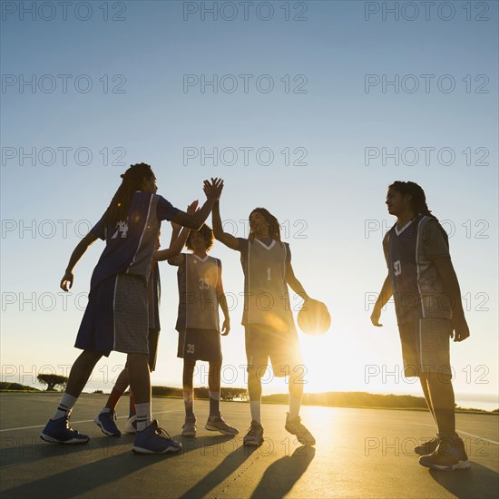 Back lit basketball team high fiving on court