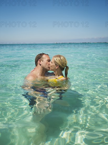 Caucasian couple kissing in water in tropical ocean