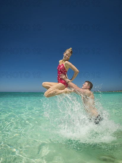 Caucasian couple playing in water in tropical ocean