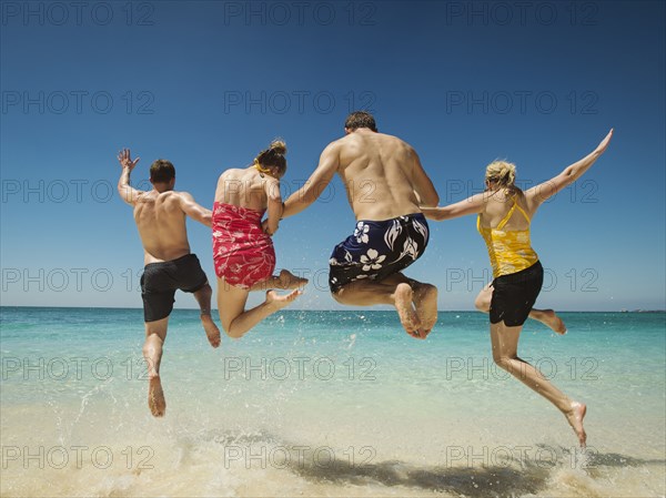 Caucasian couples jumping for joy in water on tropical beach