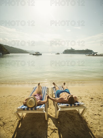 Caucasian couple holding hands in deck chairs on beach