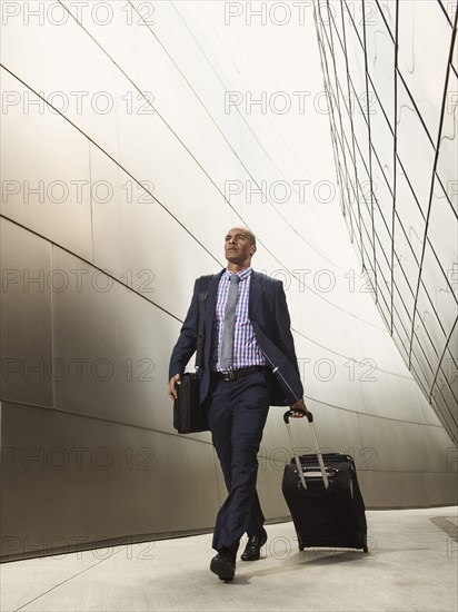 Black businessman rolling luggage