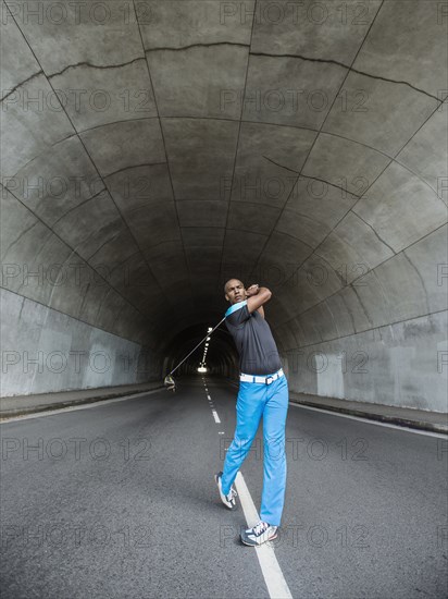 Black man playing golf in urban tunnel