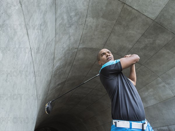 Black man playing golf in urban tunnel