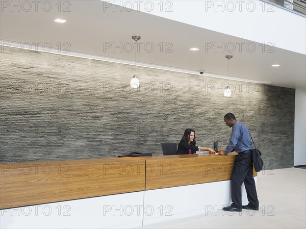 Businessman talking to receptionist at office front desk