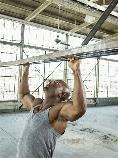 Black man doing pull-ups in warehouse