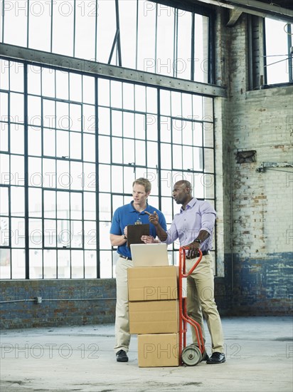 Businessmen using laptop on cardboard boxes in warehouse