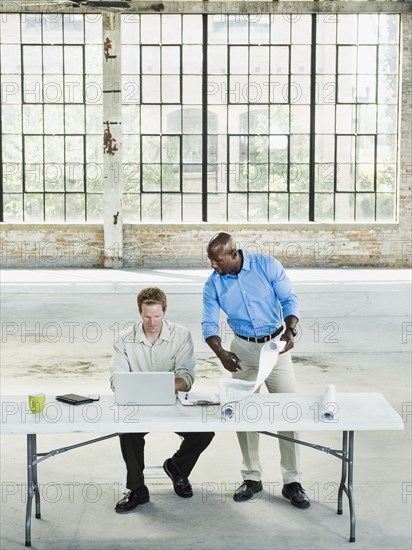 Businessmen reading blueprints in empty warehouse