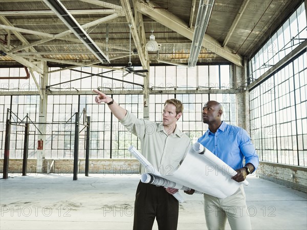 Businessmen reading blueprints in empty warehouse