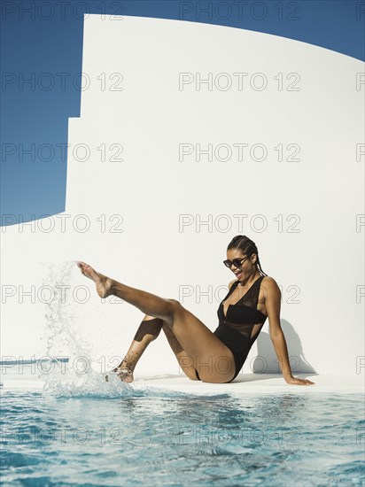 Mixed race woman in swimsuit splashing in swimming pool