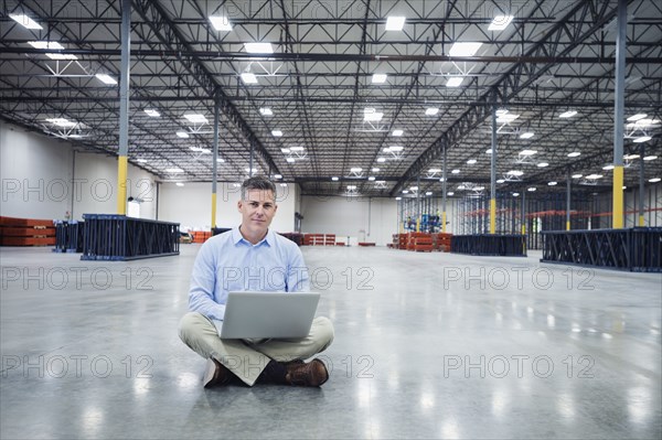 Caucasian businessman using laptop in empty warehouse