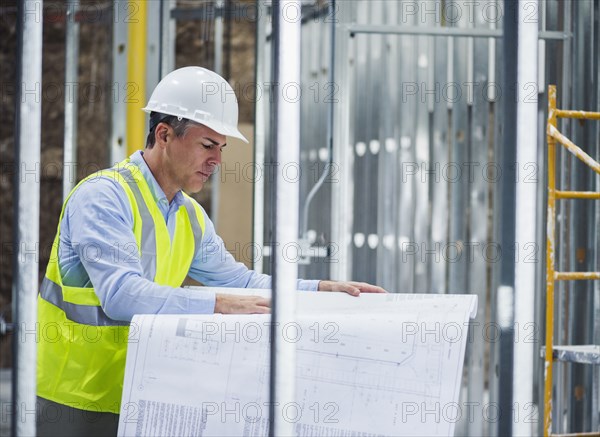 Caucasian architect reading blueprints at construction site