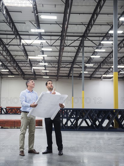 Caucasian architects reading blueprints in warehouse