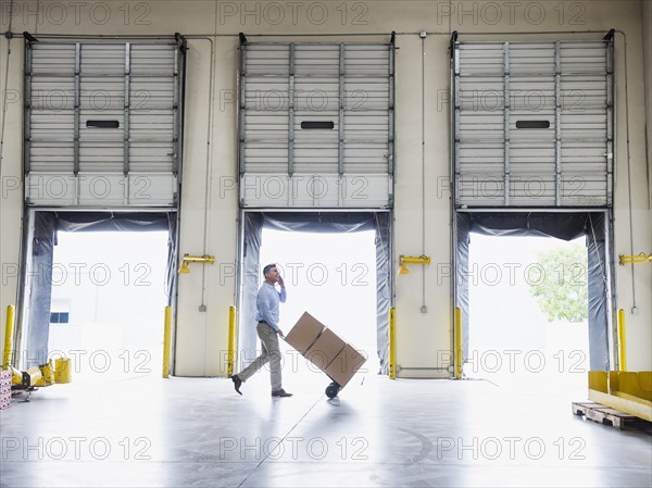 Caucasian businessman wheeling cardboard boxes in warehouse