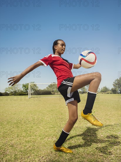 Mixed race soccer player kicking ball on field