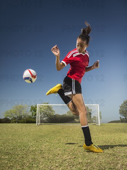 Mixed race soccer player kicking ball on field