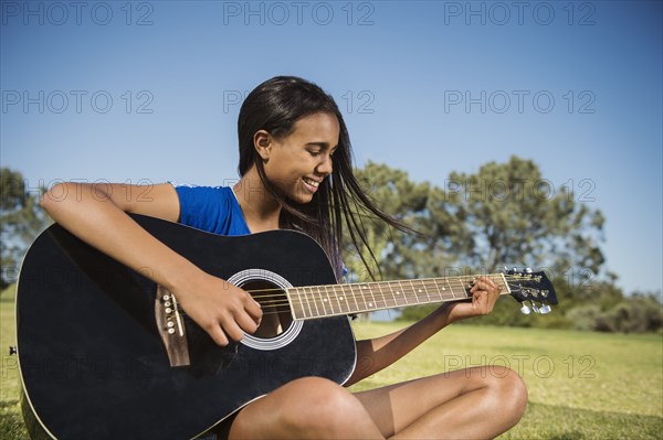 Mixed race girl playing guitar in park