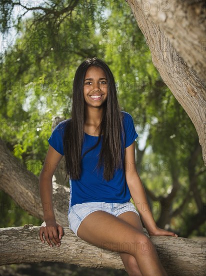 Mixed race girl sitting on tree branch