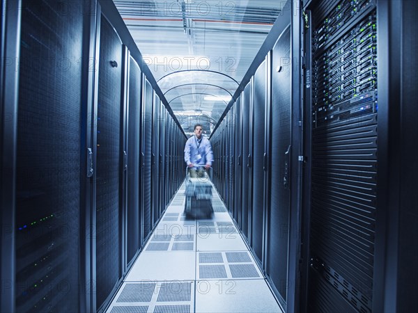 Hispanic technician pushing cart in server room