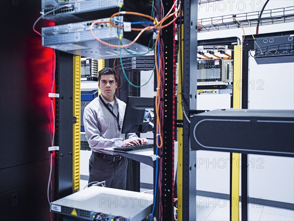 Hispanic technician using computer in server room