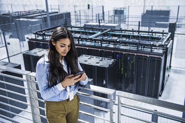 Mixed race businesswoman using cell phone on balcony over server room