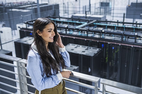 Mixed race businesswoman using cell phone on balcony over server room