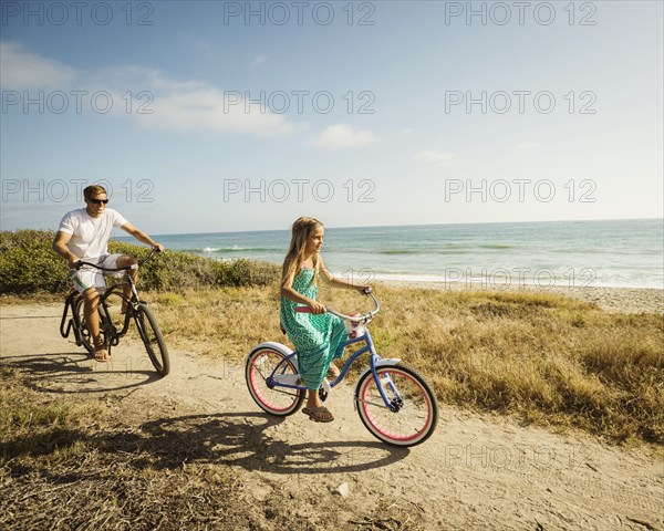 Caucasian father and daughter riding bicycles on beach