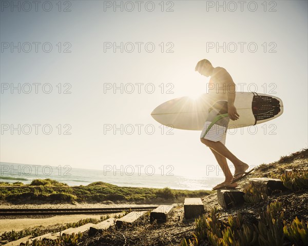 Caucasian man carrying surfboard on beach