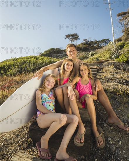 Caucasian father and daughters sitting on hillside