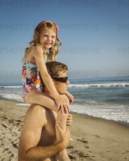 Caucasian father carrying daughter on beach